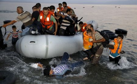Syrian refugees carry their children as they jump off an overcrowded dinghy upon arriving on a beach on the Greek island of Kos, after crossing a part of the Aegean sea from Turkey, August 9, 2015. United Nations refugee agency (UNHCR) called on Greece to take control of the "total chaos" on Mediterranean islands, where thousands of migrants have landed. About 124,000 have arrived this year by sea, many via Turkey, according to Vincent Cochetel, UNHCR director for Europe. REUTERS/Yannis Behrakis TPX IMAGES OF THE DAY - RTX1NN3R